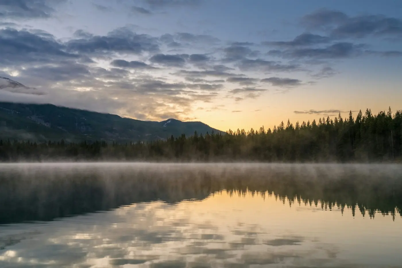 Nebliger See im Morgenlicht mit Bergen